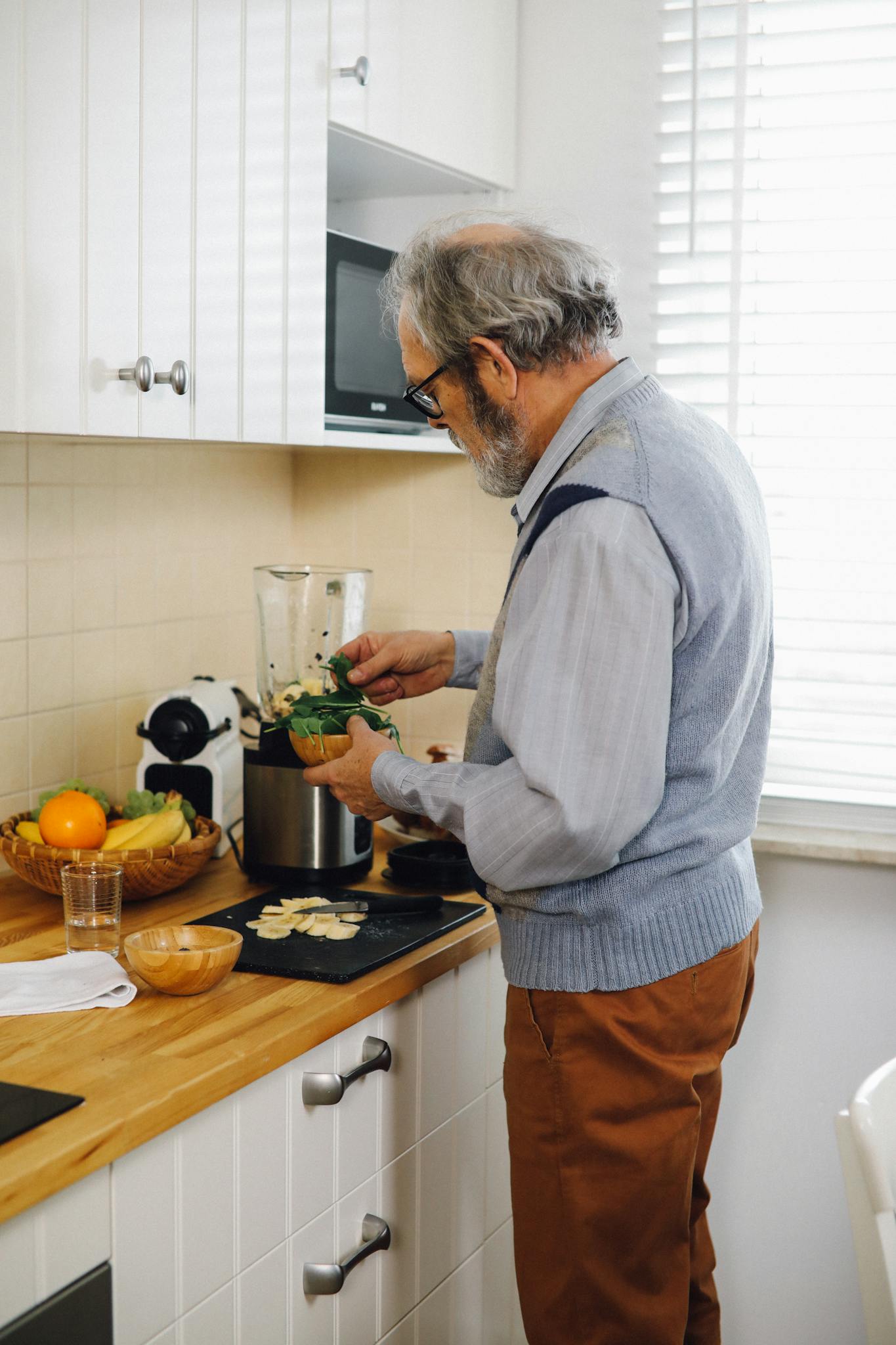 Elderly man making a green smoothie in a cozy home kitchen.