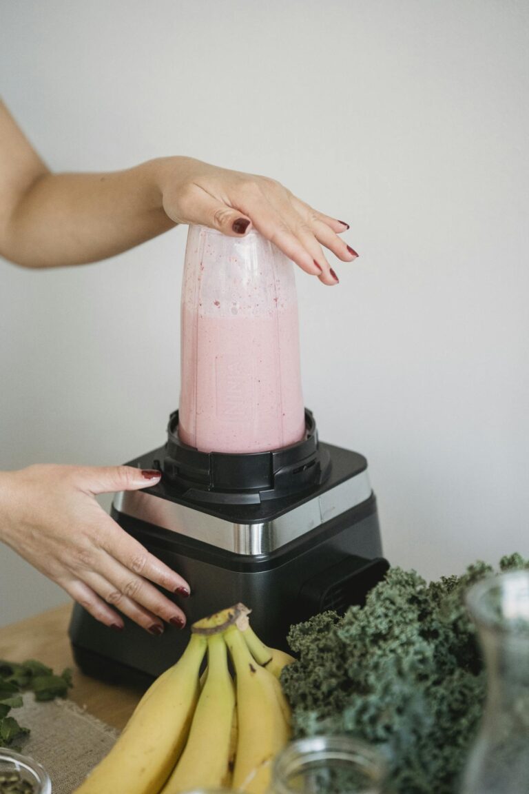 Hands making a nutritious pink smoothie with bananas and kale using a blender.
