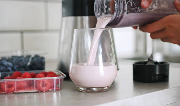 Little girl pouring a raspberry milkshake into a glass in the kitchen